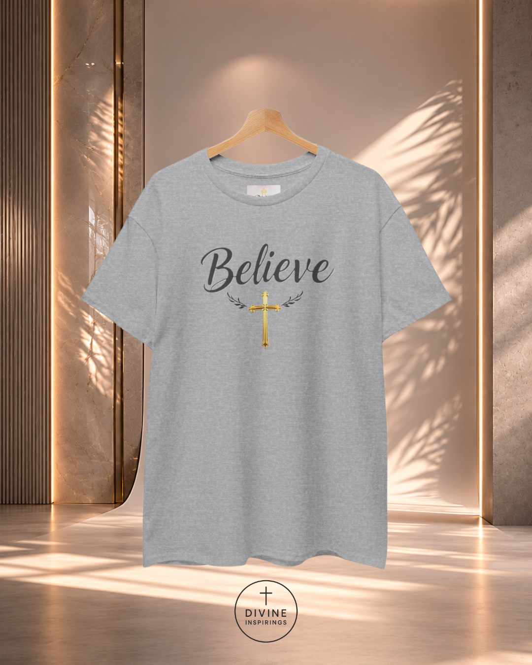 Gray t-shirt with 'Believe' and cross design on a wooden hanger against a neutral background