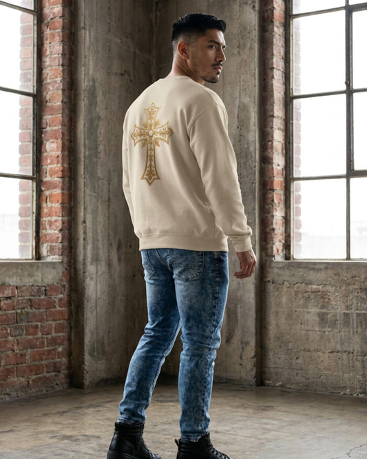Man wearing a cream sweatshirt with a gold cross design in an industrial setting.