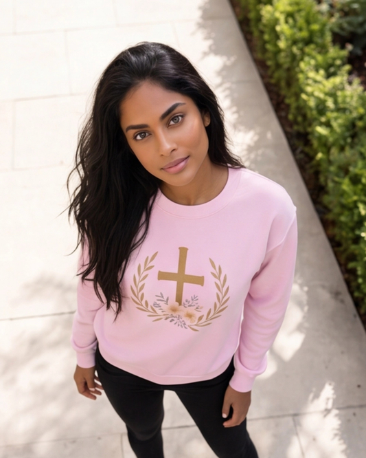 Woman wearing a pink sweatshirt with a gold cross design outdoors.