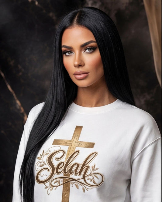 Woman wearing a white sweatshirt with a gold cross and 'Selah' design on a dark background