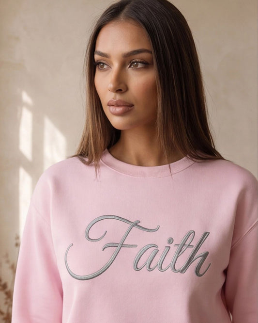 Woman wearing a pink sweatshirt with 'Faith' printed on it against a neutral background
