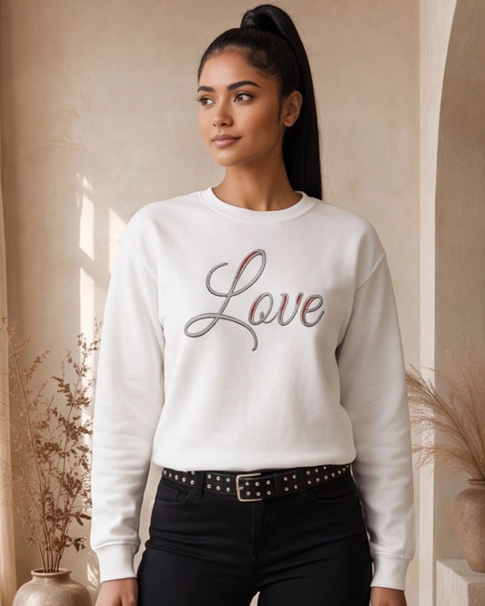 Woman wearing a white sweatshirt with 'Love' printed on it, standing indoors.