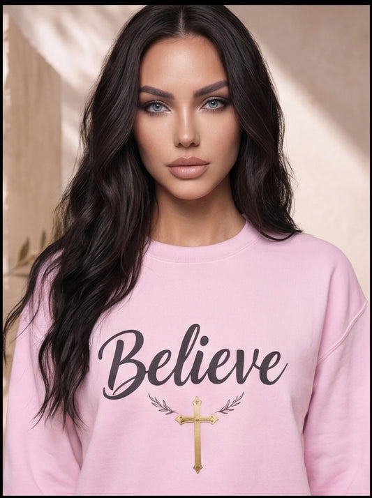 Woman wearing a pink sweatshirt with 'Believe' and a cross design.