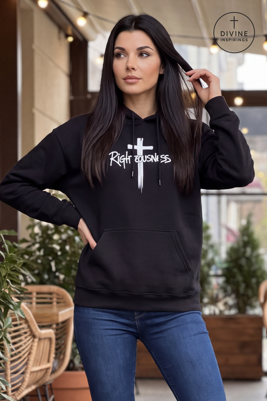 A woman wearing a black pullover hoodie with a white cross graphic and the text 'Righteousness' on the front, paired with blue jeans, standing in an outdoor patio setting.