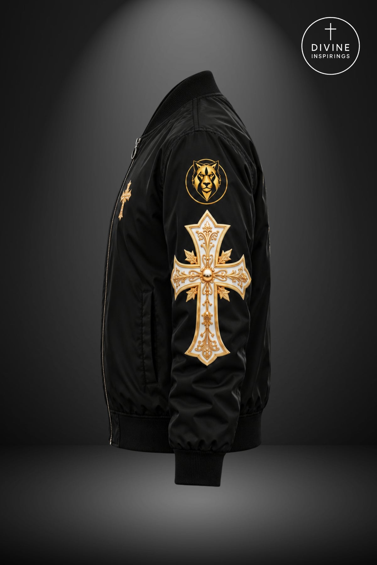 A black bomber jacket shown from the side against a dark gray gradient background, featuring a large gold cross patch with rhinestones on the right sleeve and a gold lion emblem on the upper left sleeve. A circular 'DIVINE INSPIRINGS' logo is visible in the top right corner.