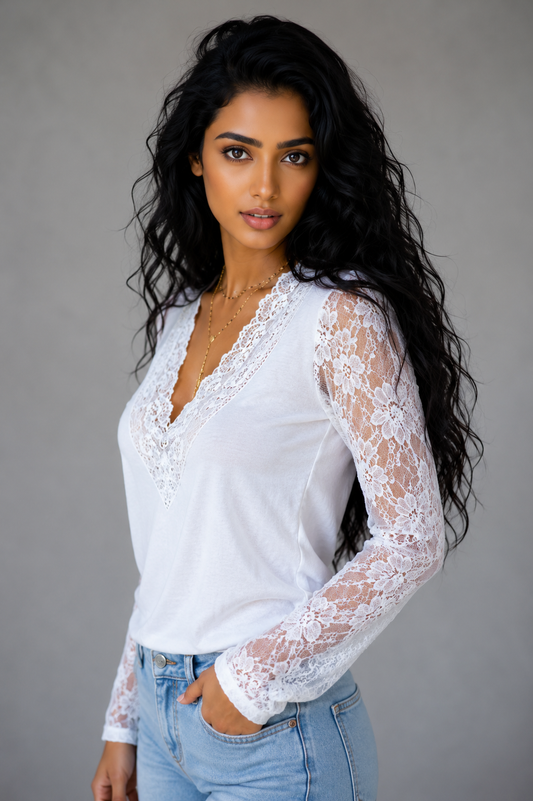 Woman wearing a white lace long-sleeve top and blue jeans against a gray background