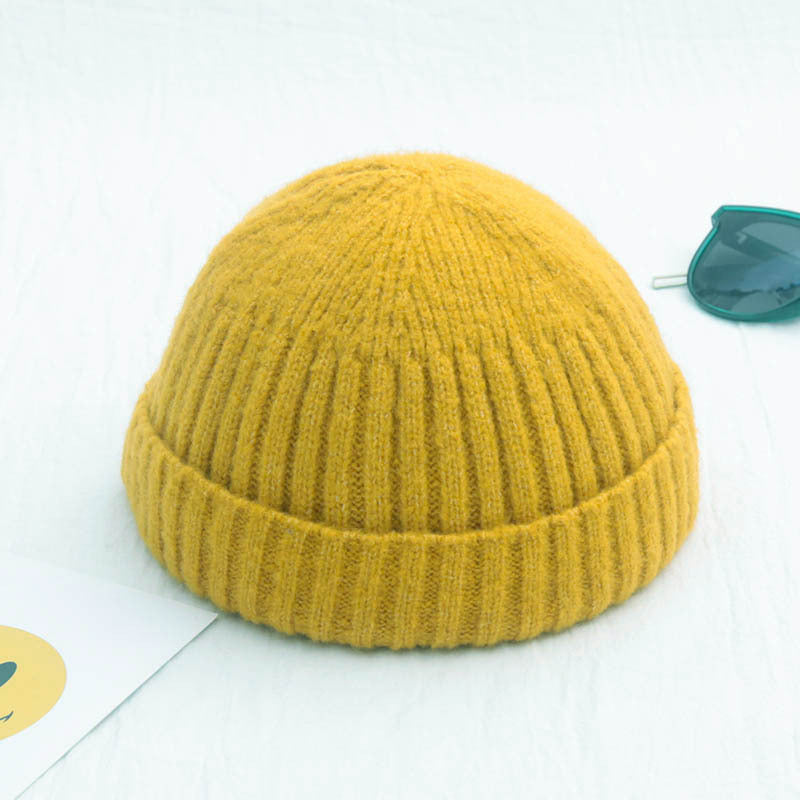 Yellow knit beanie on a white surface with a small green object in the background