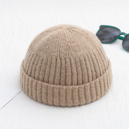 Beige knit beanie on a white background with sunglasses in the corner.