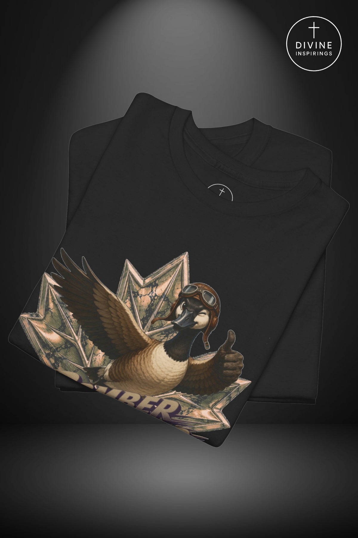 A black folded t-shirt displayed against a dark gray background with a spotlight effect. The front of the shirt features a large graphic print of a goose wearing aviator goggles and holding a thumbs-up, emerging from a stack of dollar bills.