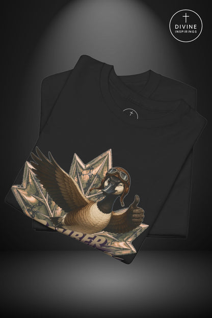 A black folded t-shirt displayed against a dark gray background with a spotlight effect. The front of the shirt features a large graphic print of a goose wearing aviator goggles and holding a thumbs-up, emerging from a stack of dollar bills.