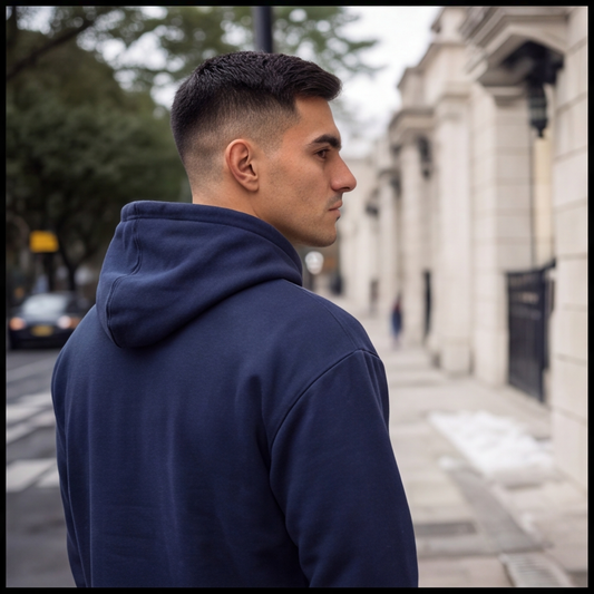A man wearing a navy blue hoodie, shown from a side-back angle in an outdoor urban setting with a blurred street and building in the background.