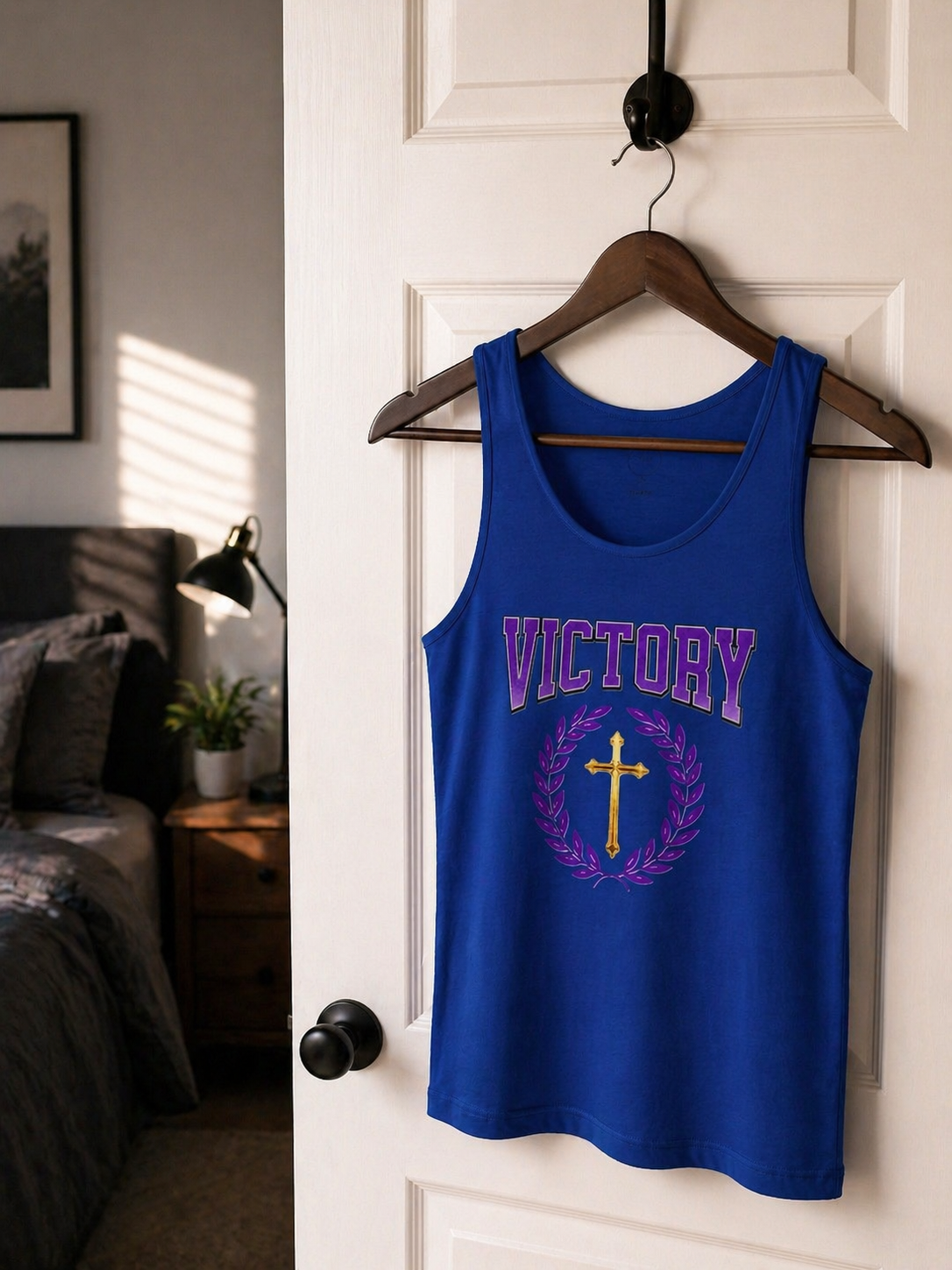 Blue tank top with 'VICTORY' and cross design on a hanger against a white door.