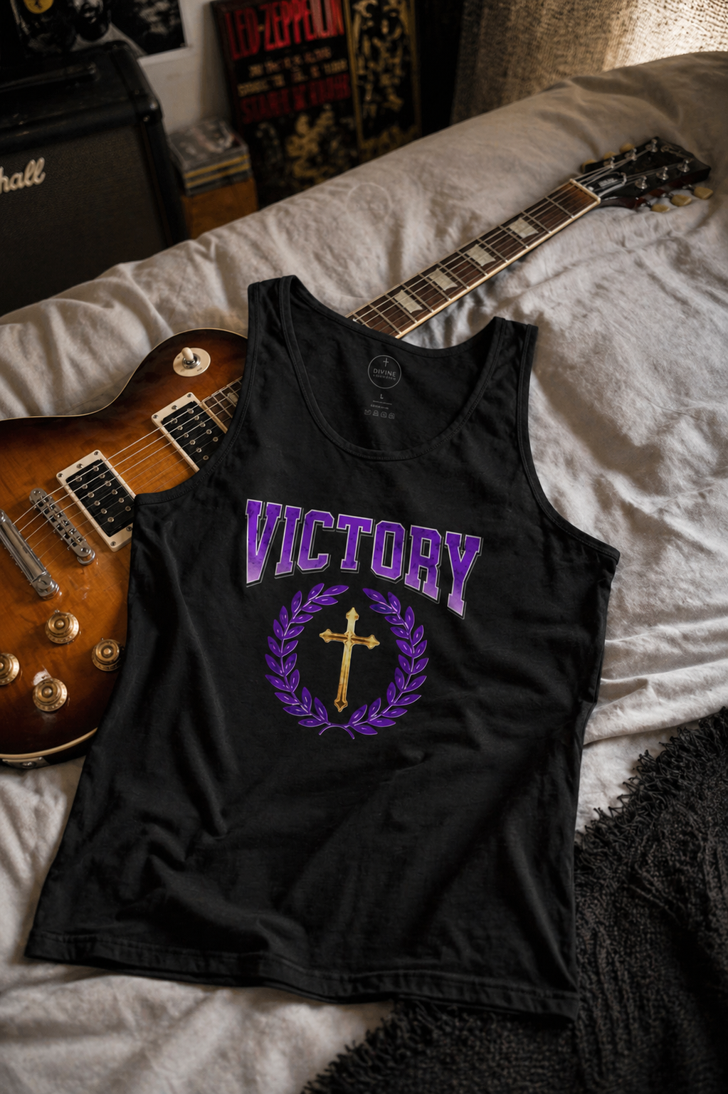 Black tank top with 'VICTORY' design on a bed with a guitar
