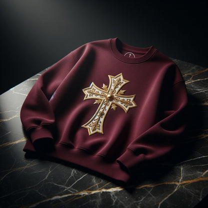 Maroon sweatshirt with a gold cross design on a dark marble surface