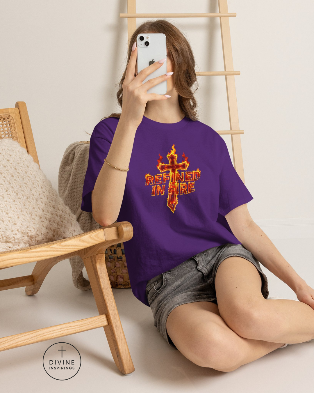Person wearing a purple t-shirt with a logo and text, sitting on the floor with a wooden chair and ladder in the background.