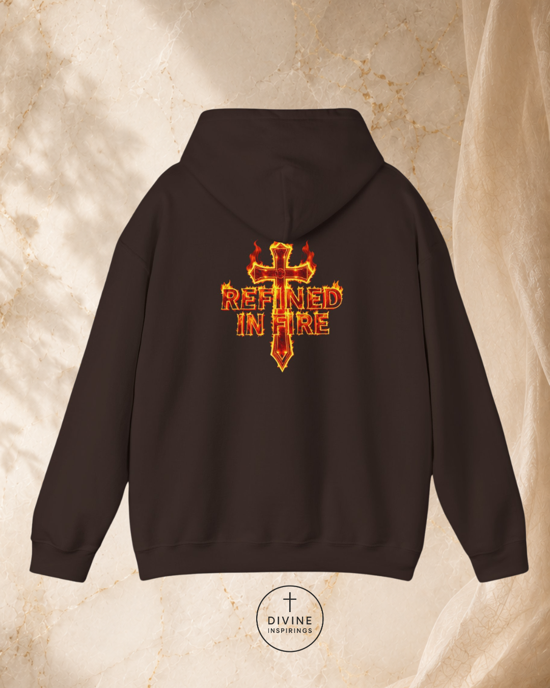 Black hoodie with a fiery cross design and 'Refined in Fire' text on the back, against a beige marble background.