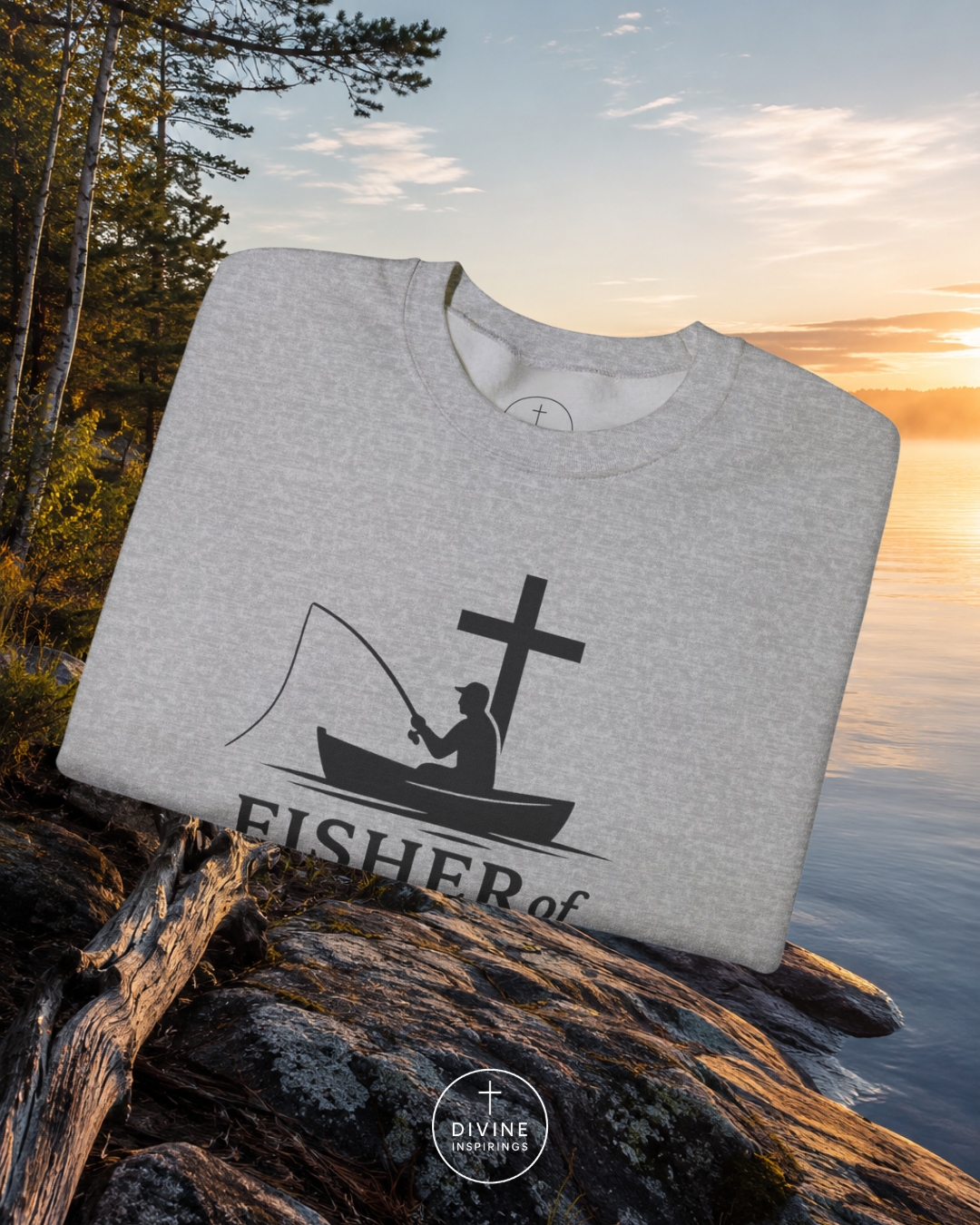 Gray sweatshirt with a fishing graphic and 'Fisher of Men' text on a rock by a lake with sunset.