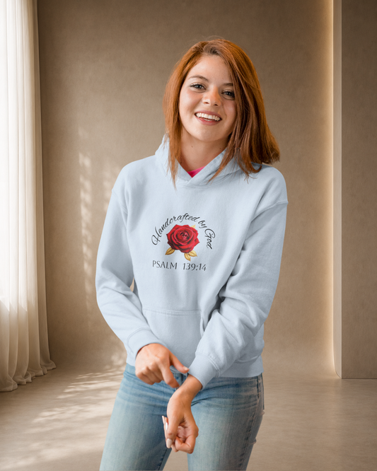 Woman wearing a light blue hoodie with a rose design and text, standing in a softly lit room.