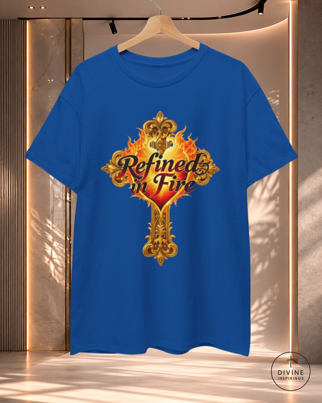 Blue t-shirt with 'Refined in Fire' design on a hanger against a neutral background