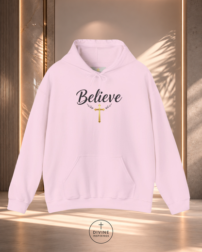 Pink hoodie with 'Believe' text and cross design on a reflective surface.