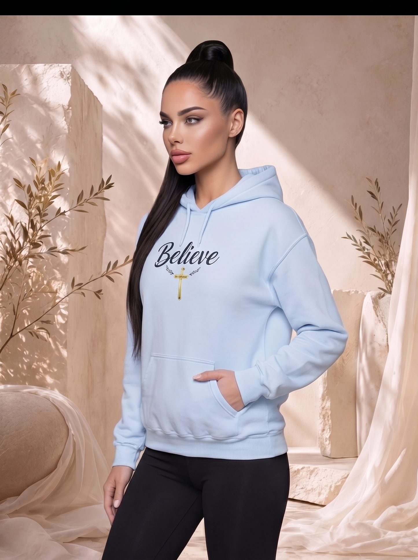 Woman wearing a light blue hoodie with 'Believe' text and a cross, standing in a softly lit room with decorative plants.