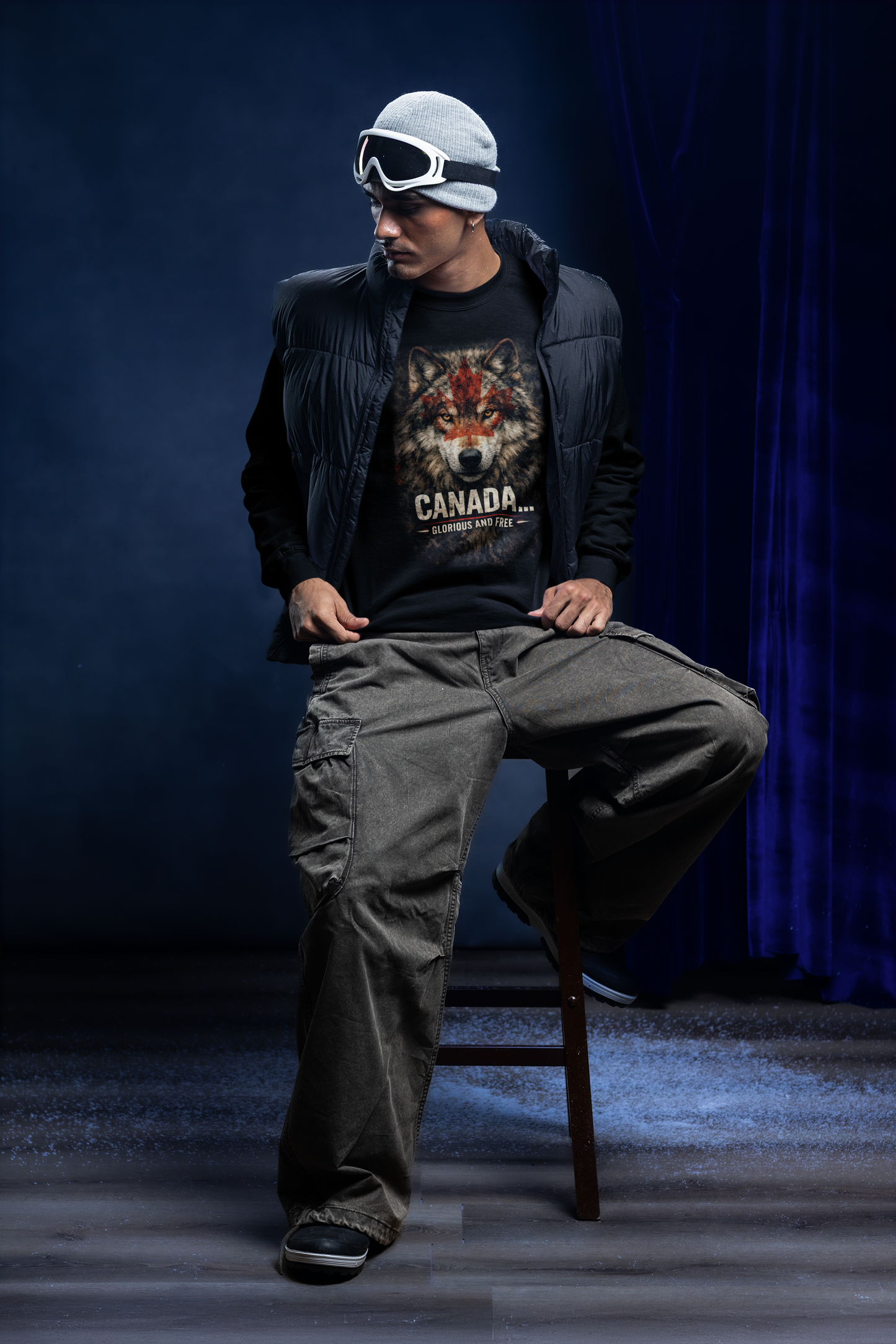Person wearing a jacket with a wolf graphic and 'Canada' text, sitting on a chair against a dark blue curtain.