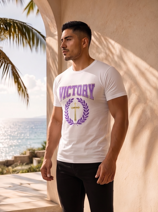 Man wearing a white t-shirt with 'VICTORY' printed on it, standing by a beach.