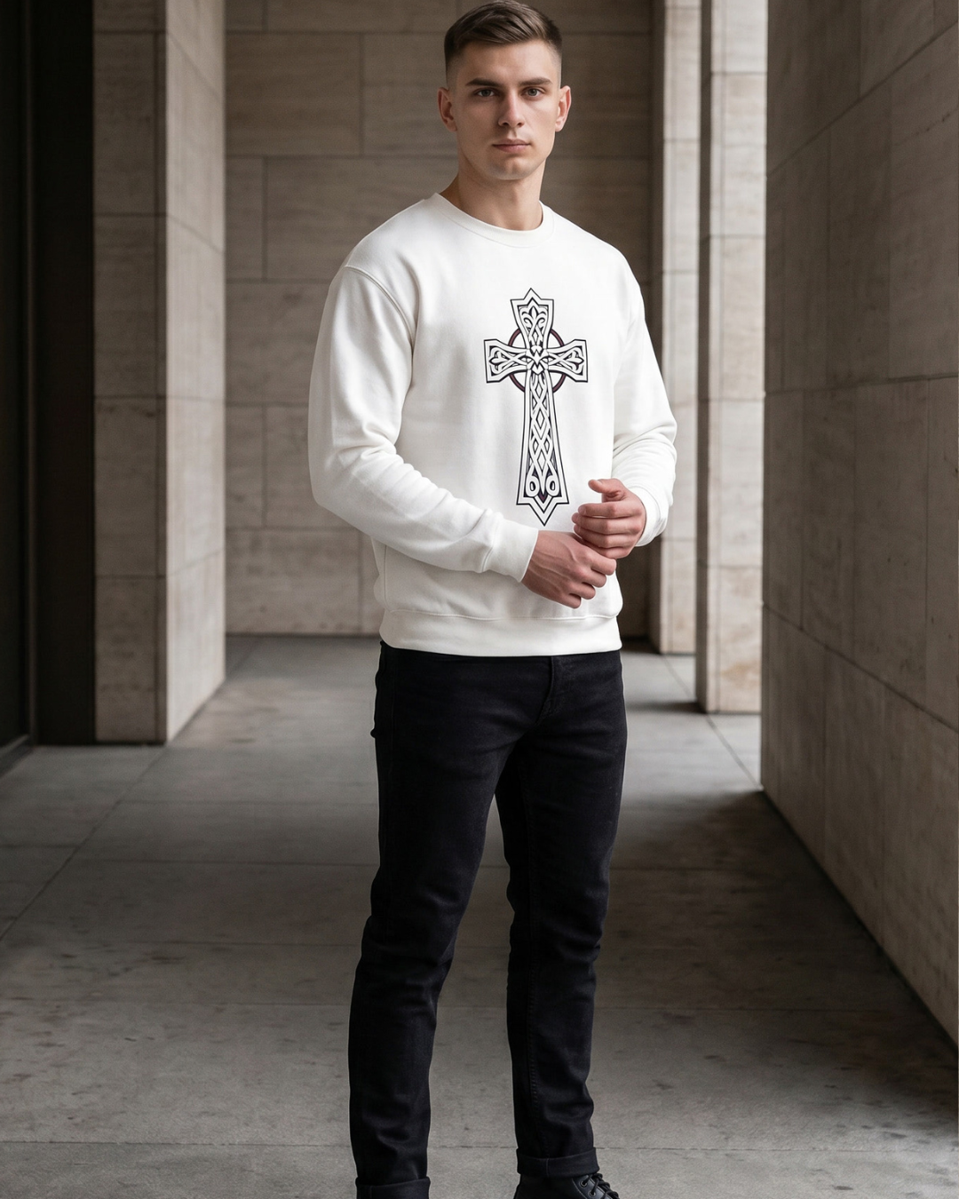 Man wearing a white sweatshirt with a black cross design in an architectural setting