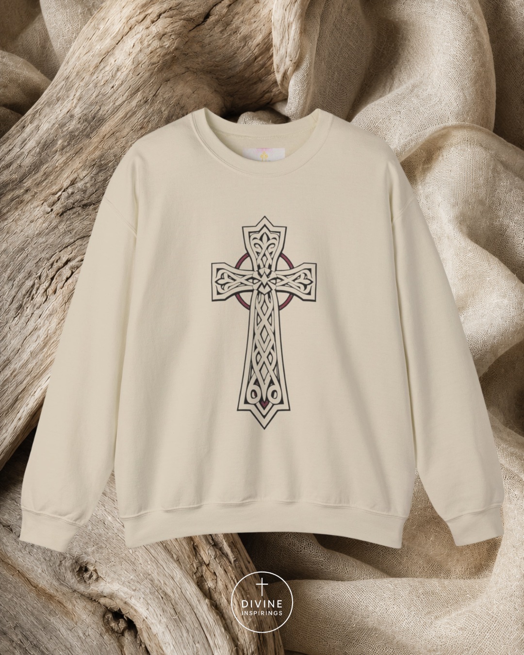 Beige sweatshirt with a Celtic cross design on a wooden surface, featuring the brand 'Divine Emporium'.