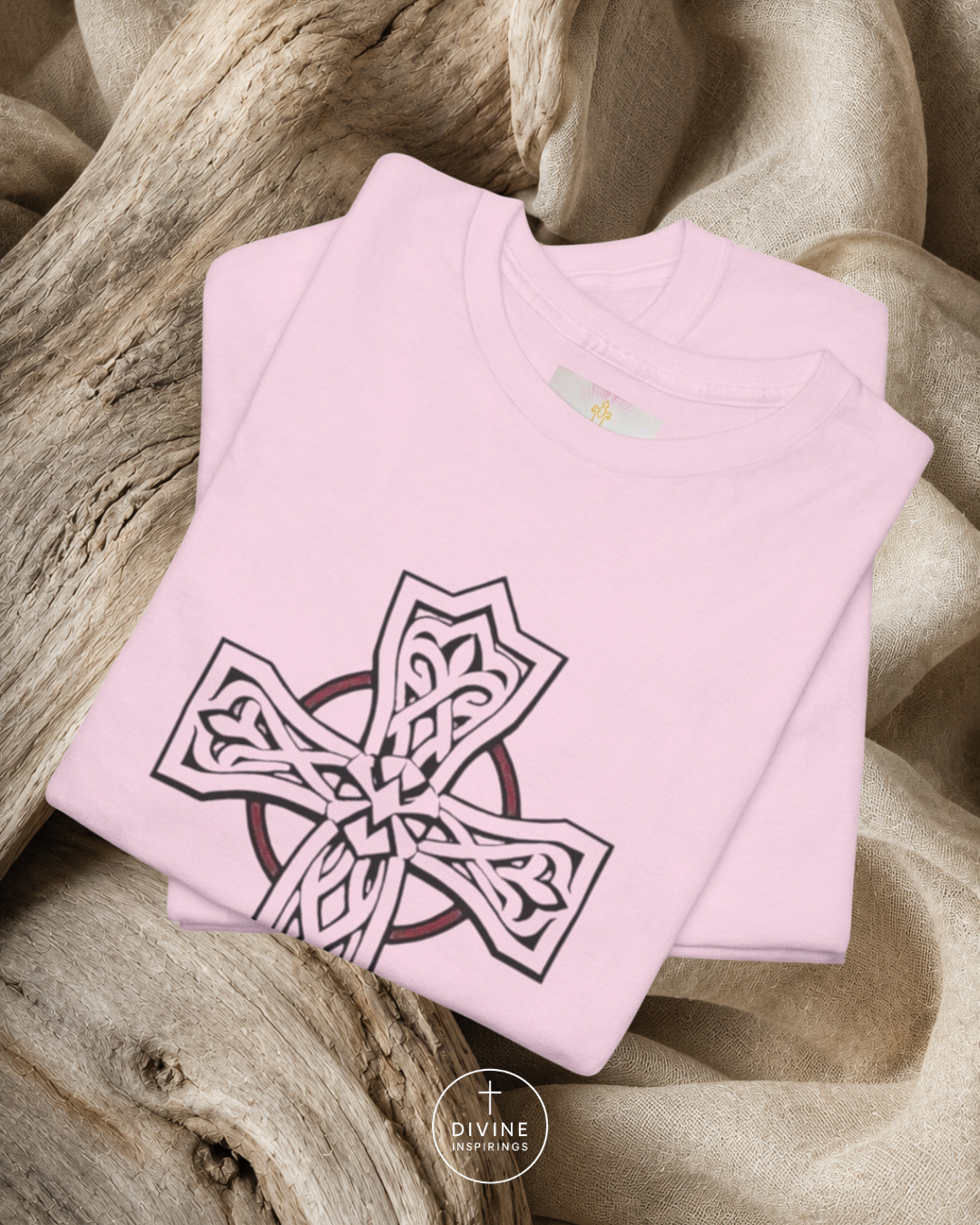 Folded pink sweatshirt with a Celtic cross design on a textured surface