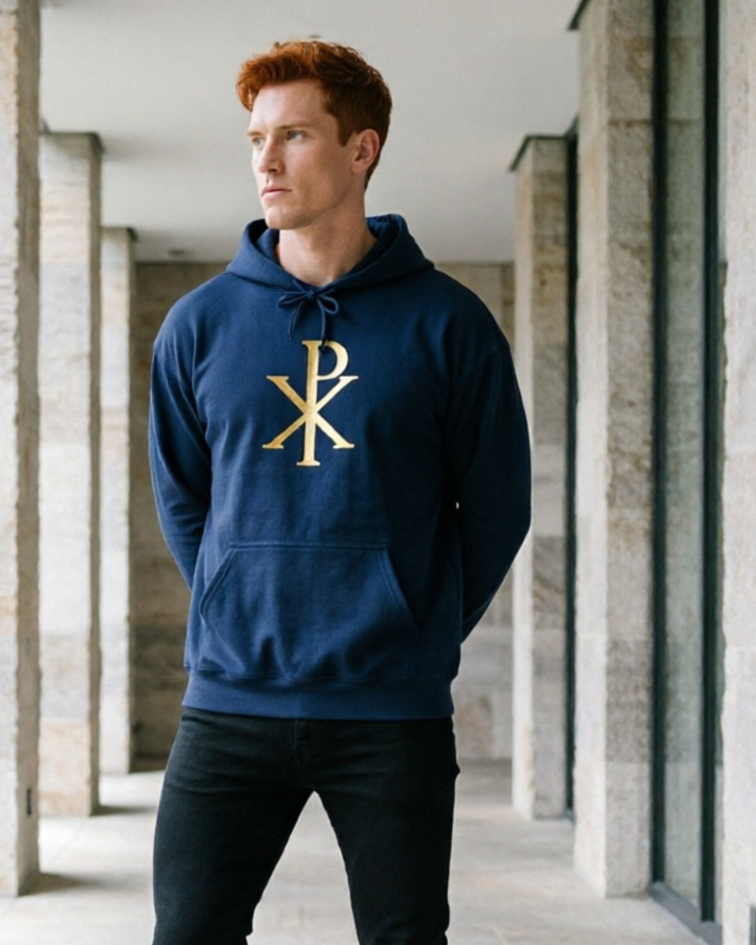 Man wearing a navy hoodie with a gold logo in an architectural setting