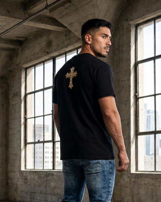 Man wearing a black t-shirt with a gold cross on the back in an industrial setting.