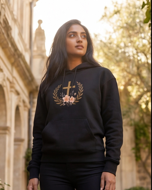 Woman wearing a black hoodie with a floral and cross design outdoors.