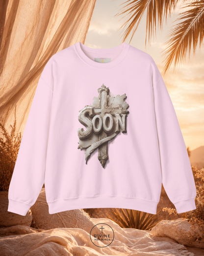 Pink sweatshirt with 'Soon' design against a warm, blurred natural background
