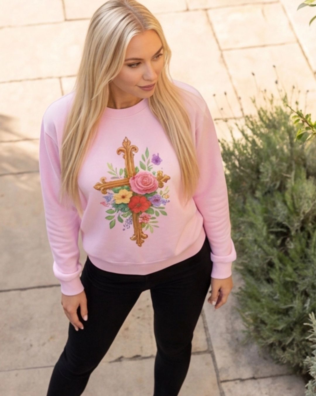 Woman wearing a pink sweatshirt with a floral cross design outdoors.