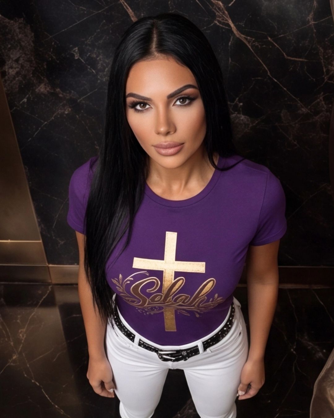 Woman wearing a purple t-shirt with a gold cross and text design against a dark marble wall.