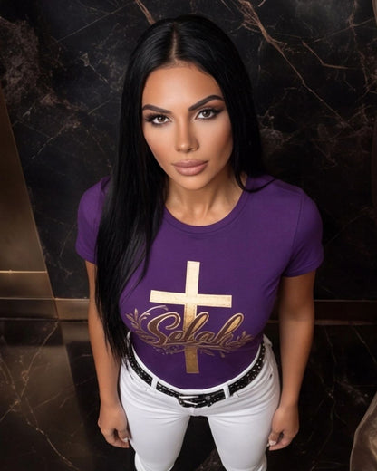 Woman wearing a purple t-shirt with a gold cross and text design against a dark marble wall.