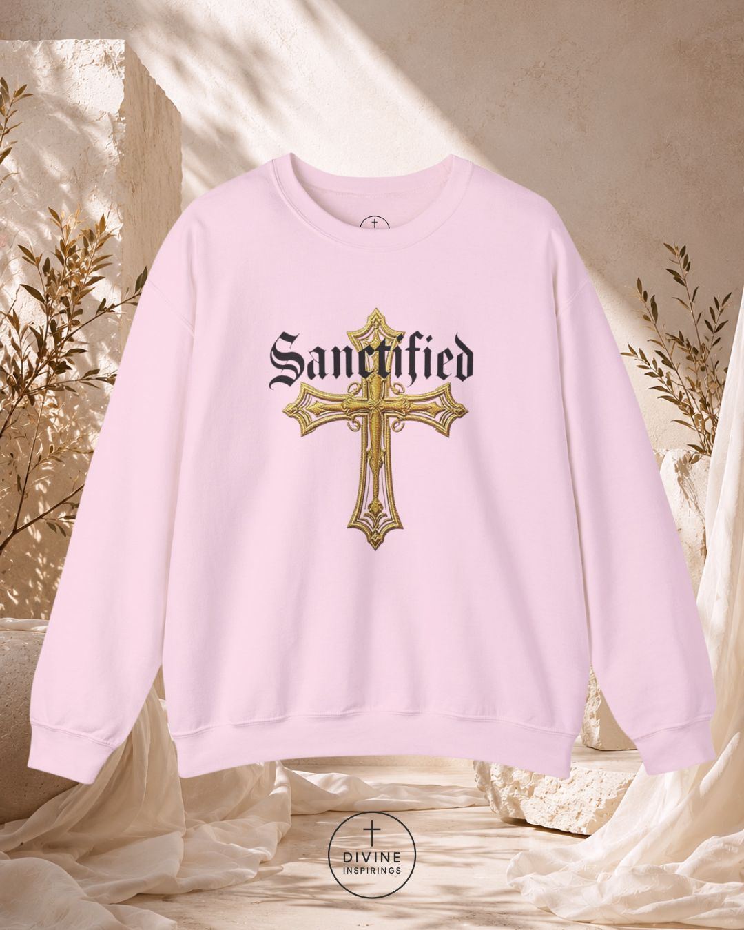 Pink sweatshirt with gold cross and 'Sanctified' text on a neutral background