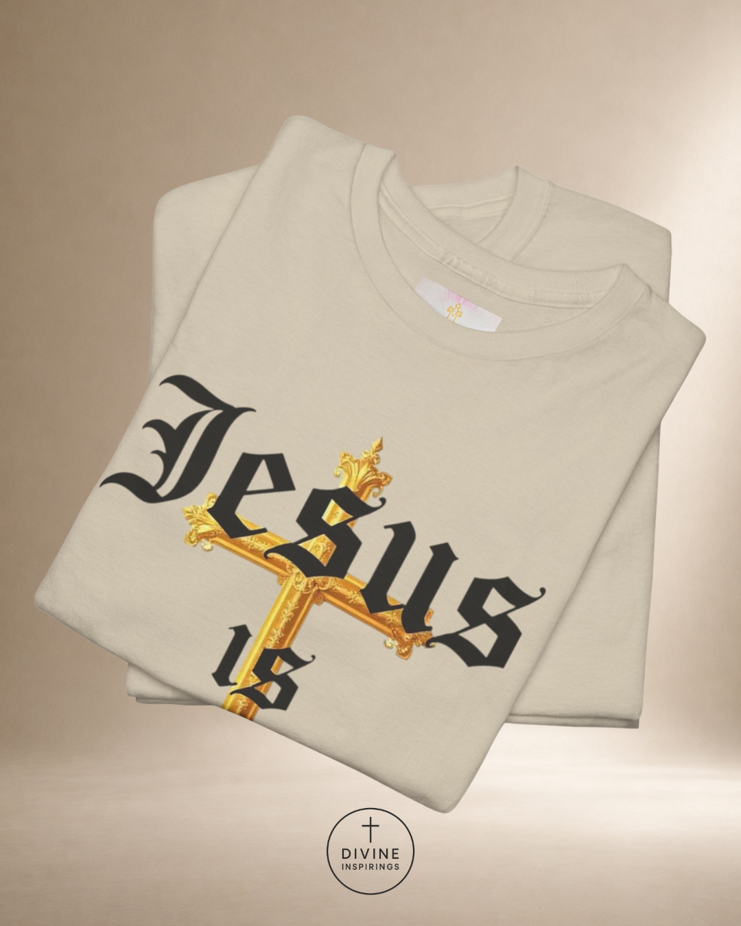Folded beige sweatshirt with 'Jesus is' text and cross design on a beige background