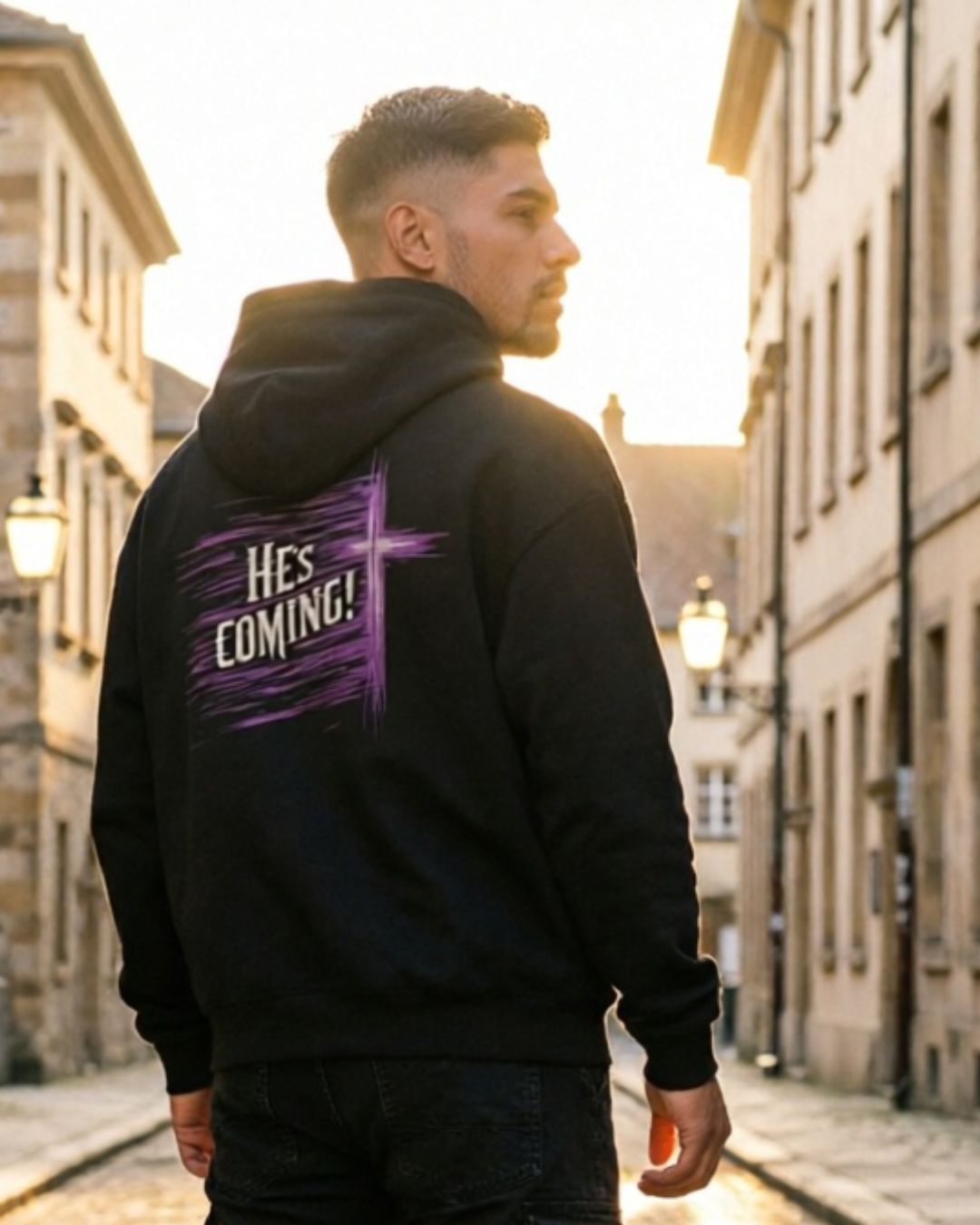 Person wearing a black hoodie with 'He's Coming!' text on the back, standing in an urban street setting.