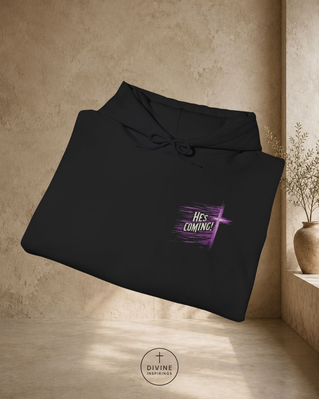 Black hoodie with 'HE'S COMING!' text on a beige wall background