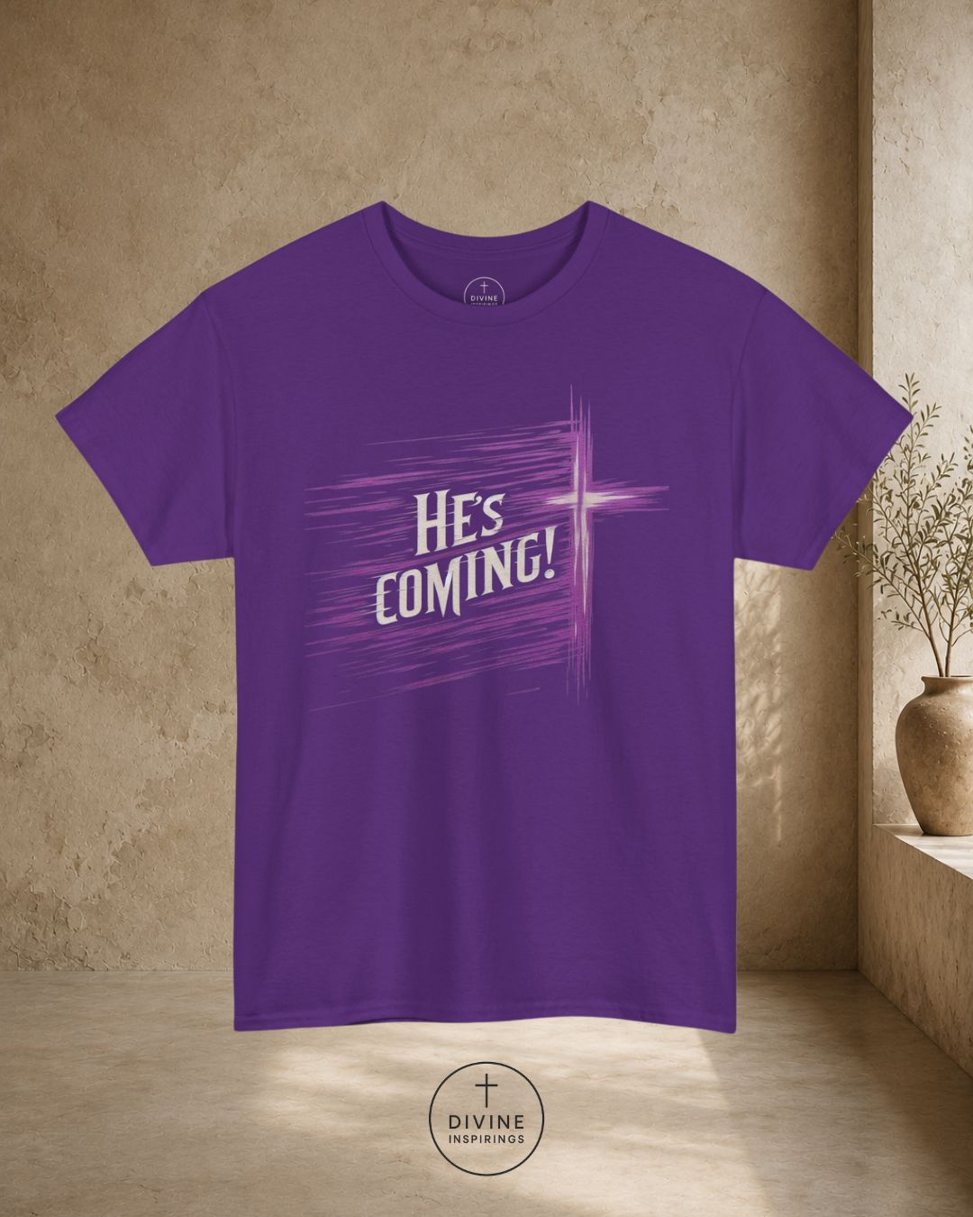 Purple t-shirt with 'HE'S COMING!' text on a beige wall background