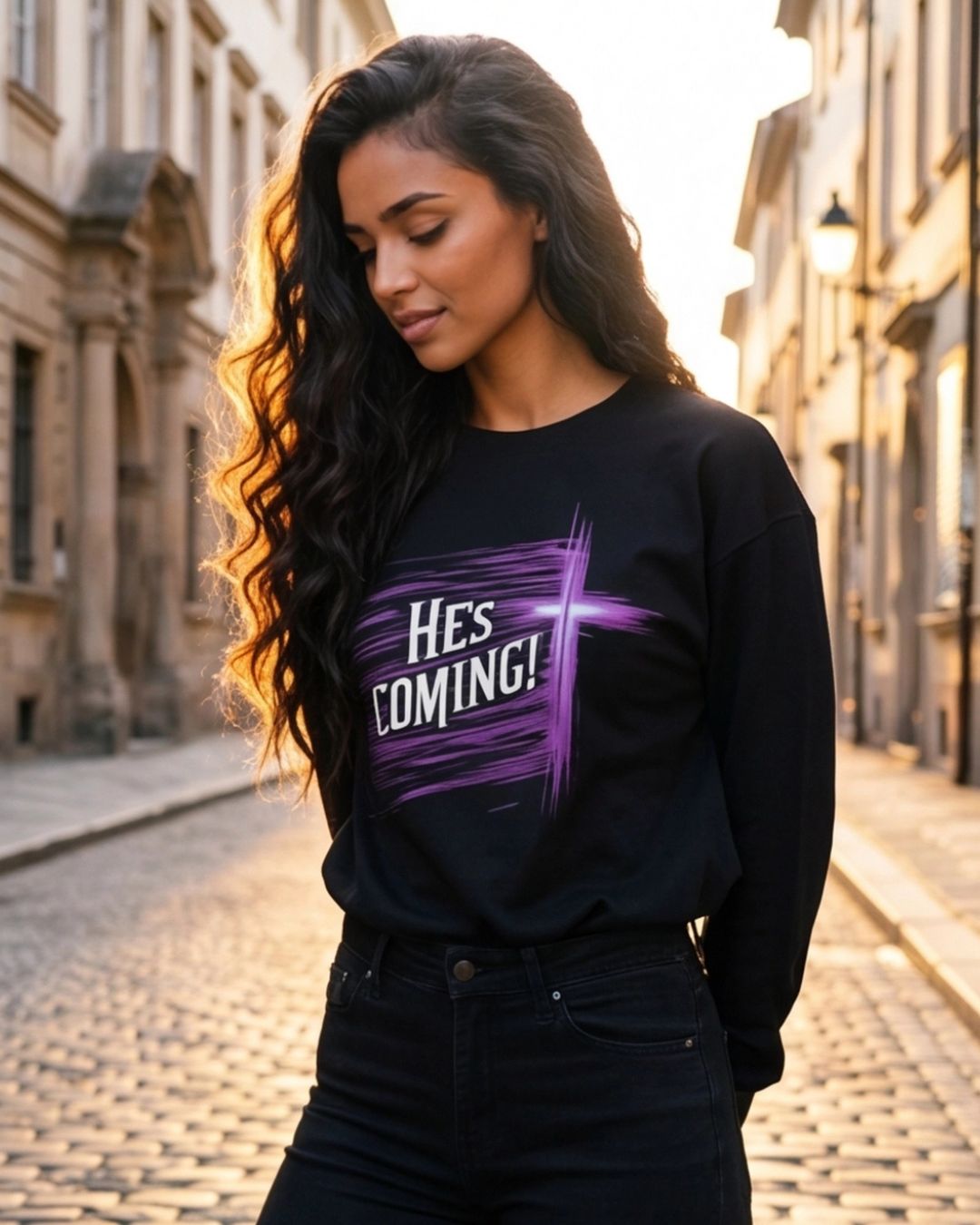 Woman wearing a black sweatshirt with 'HE'S COMING!' text on a cobblestone street.