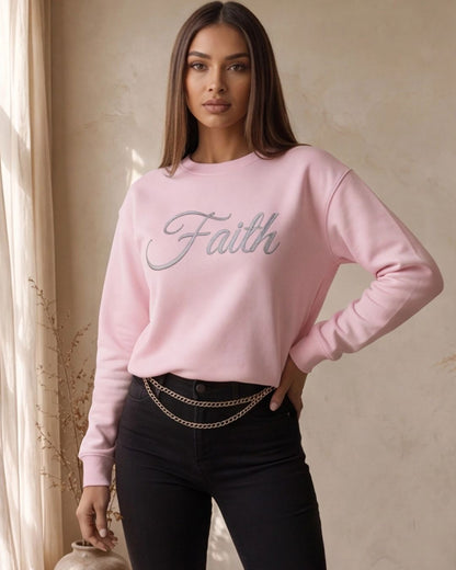 Woman wearing a pink sweatshirt with 'Faith' text, standing indoors against a neutral wall.