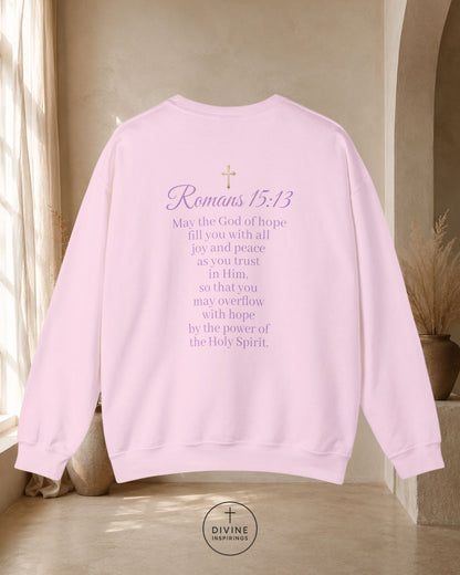 Pink sweatshirt with 'Romans 15:13' text in a home setting