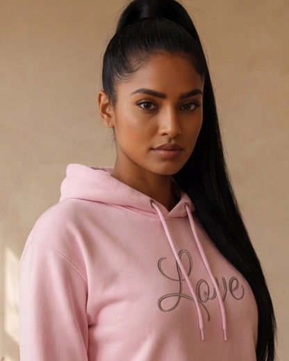Woman wearing a pink hoodie with 'Love' printed on it against a beige background