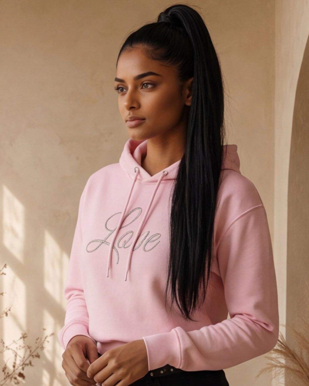 Person wearing a pink hoodie with 'Love' text, standing against a beige wall.