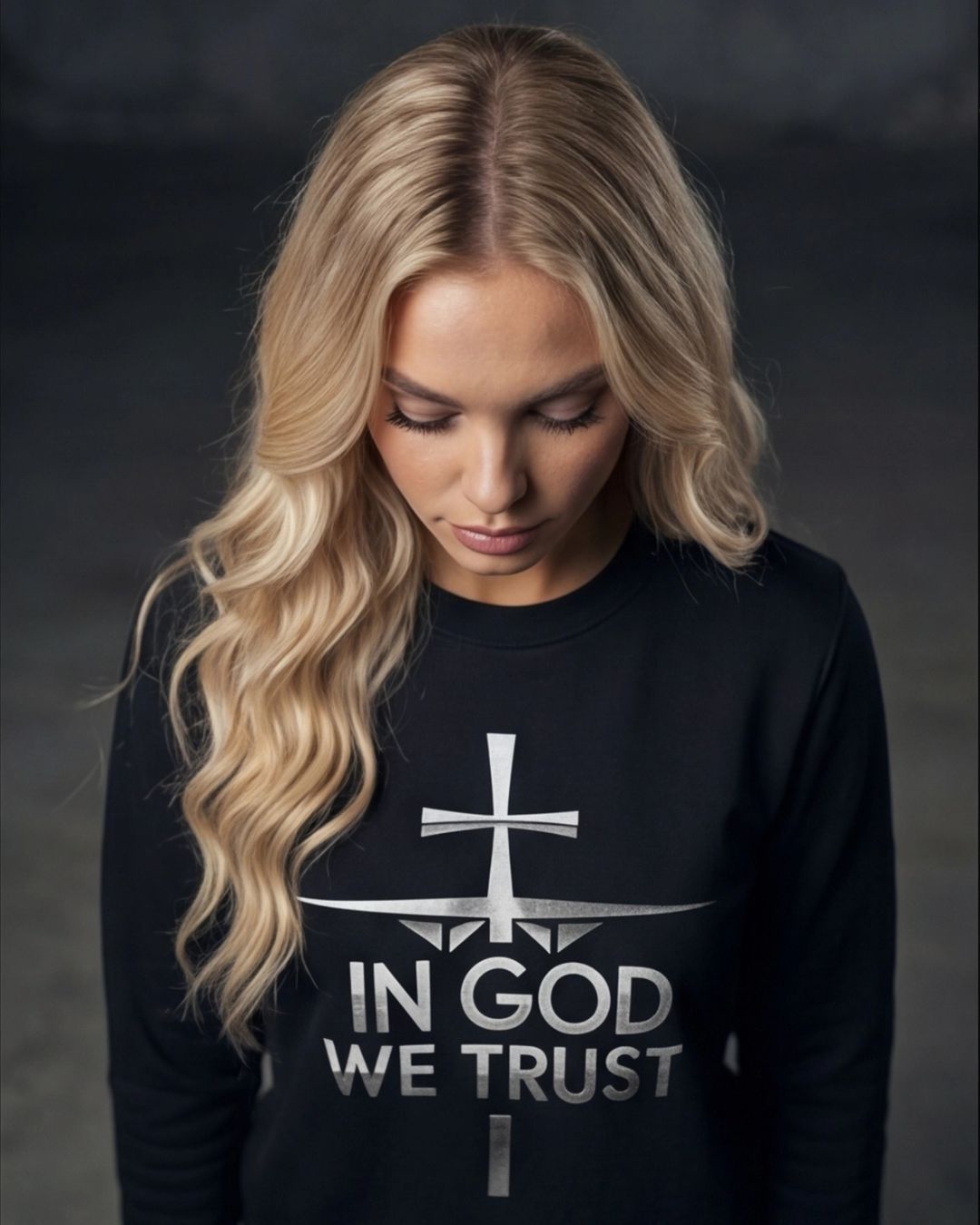 Woman wearing a black sweatshirt with 'In God We Trust' text and cross design on a dark background