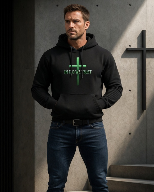 Man wearing a black hoodie with a green cross design and text, standing against a concrete wall.
