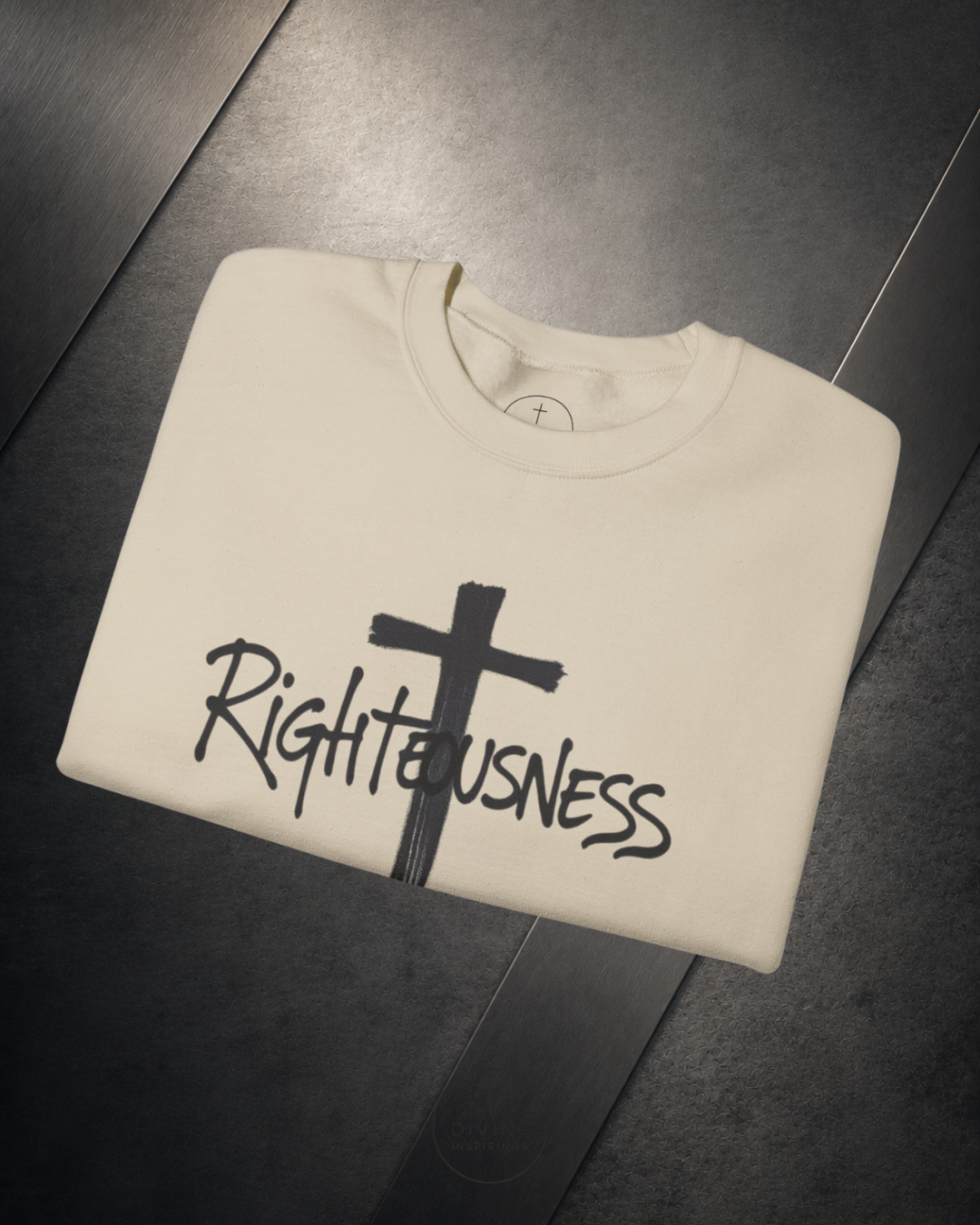 Folded beige sweatshirt with a black cross and 'Righteousness' text on a dark surface